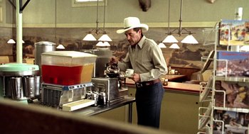 Movie still from “U Turn” (1997), directed by Oliver Stone – A man wearing a cowboy hat is making a cup of coffee; Medium shot, Low angle