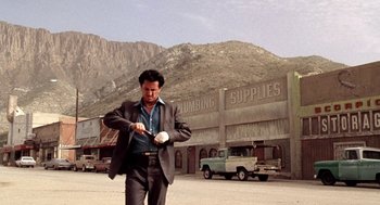 Movie still from “U Turn” (1997), directed by Oliver Stone – A man in a suit and tie holding a watch; Wide shot, Low angle