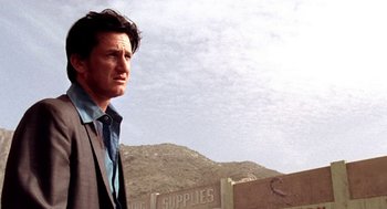 Movie still from “U Turn” (1997), directed by Oliver Stone – A man standing in front of a building on a hill; Close Up shot, Low angle