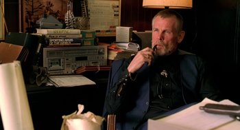 Movie still from “U Turn” (1997), directed by Oliver Stone – An older man sitting in a chair in front of a desk; Close Up shot, Over the shoulder angle