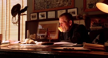 Movie still from “U Turn” (1997), directed by Oliver Stone – An older man sitting at a table with papers; Medium shot, Low angle