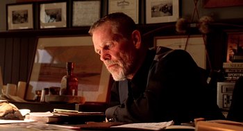 Movie still from “U Turn” (1997), directed by Oliver Stone – An older man sitting at a table with papers and a bottle; Close Up shot, Low angle