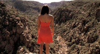 Movie still from “U Turn” (1997), directed by Oliver Stone – A woman in a red dress standing on top of a mountain; Extreme Wide shot, High angle