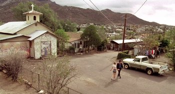 Movie still from “U Turn” (1997), directed by Oliver Stone – Two people walking down a street near a house; Extreme Wide shot, High angle