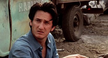 Movie still from “U Turn” (1997), directed by Oliver Stone – A person sitting on the ground near a truck; Close Up shot, Over the shoulder angle