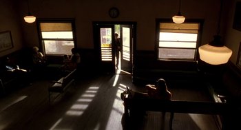 Movie still from “U Turn” (1997), directed by Oliver Stone – People sitting on benches in front of an open door; Wide shot, Low angle