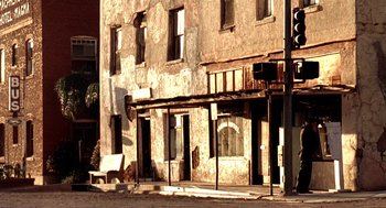Movie still from “U Turn” (1997), directed by Oliver Stone – An old building with a bench sitting on the side of the street; Extreme Wide shot, Low angle