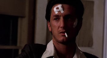 Movie still from “U Turn” (1997), directed by Oliver Stone – A man with a cigarette in his mouth and a sticker on his forehead; Close Up shot, Low angle