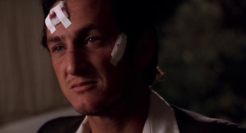 Movie still from “U Turn” (1997), directed by Oliver Stone – A person with bandaids on their face; Close Up shot, Low angle