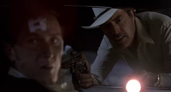 Movie still from “U Turn” (1997), directed by Oliver Stone – A man with a gun and another man with a hat; Close Up shot, Over the shoulder angle