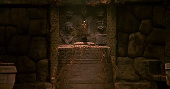 Movie still from “UHF” (1989), directed by Jay Levey – A statue of a person sitting on top of a stone pillar; Wide shot, Overhead angle
