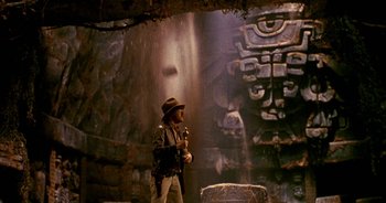 Movie still from “UHF” (1989), directed by Jay Levey – A man in a hat holding a gun in front of a statue; Wide shot, Low angle