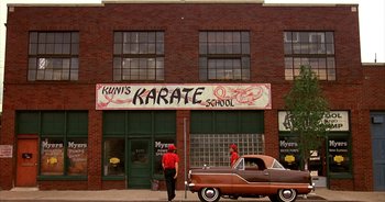 Movie still from “UHF” (1989), directed by Jay Levey – A man standing in front of a karate school; Wide shot, Low angle