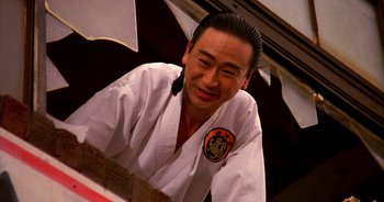 Movie still from “UHF” (1989), directed by Jay Levey – A man in a karate uniform sitting in front of a table; Close Up shot, Low angle