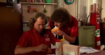 Movie still from “UHF” (1989), directed by Jay Levey – Two men sitting at a table eating a sandwich; Medium shot, Over the shoulder angle