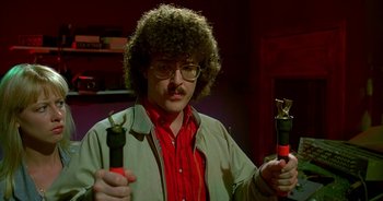 Movie still from “UHF” (1989), directed by Jay Levey – A man holding a pair of pliers in one hand and a pair of scissors in the other hand; Close Up shot, Low angle