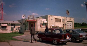 Movie still from “UHF” (1989), directed by Jay Levey – A man walking down the street next to a car; Wide shot, Low angle