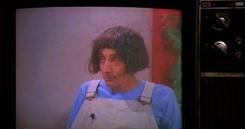 Movie still from “UHF” (1989), directed by Jay Levey – A man with long black hair wearing an overalls; Close Up shot, High angle
