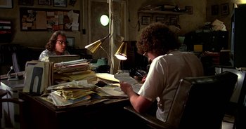 Movie still from “UHF” (1989), directed by Jay Levey – Two people sitting at a table with papers; Wide shot, High angle