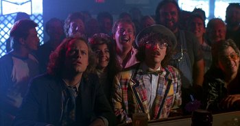 Movie still from “UHF” (1989), directed by Jay Levey – A group of people sitting in front of an audience; Medium shot, Over the shoulder angle