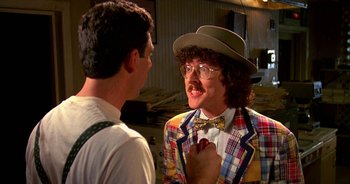 Movie still from “UHF” (1989), directed by Jay Levey – A man in a plaid jacket and a hat is talking to another man in a plaid jacket; Medium shot, Over the shoulder angle