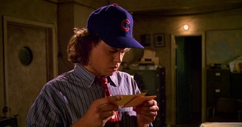 Movie still from “UHF” (1989), directed by Jay Levey – A man in a baseball cap looking down at a piece of paper; Close Up shot, Over the shoulder angle