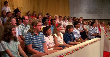 Movie still from “UHF” (1989), directed by Jay Levey – A group of people sitting in front of each other on a stage; Wide shot, Over the shoulder angle