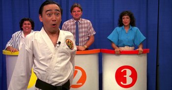 Movie still from “UHF” (1989), directed by Jay Levey – A man in a karate outfit standing in front of two other people; Medium shot, Over the shoulder angle