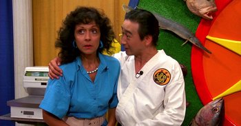 Movie still from “UHF” (1989), directed by Jay Levey – A man and a woman standing next to each other; Close Up shot, Over the shoulder angle