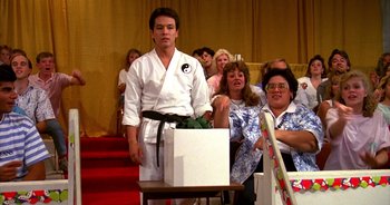 Movie still from “UHF” (1989), directed by Jay Levey – A man standing in front of a group of people; Medium shot, Over the shoulder angle