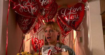 Movie still from “UHF” (1989), directed by Jay Levey – A woman standing in front of a bunch of heart shaped balloons; Medium shot, High angle