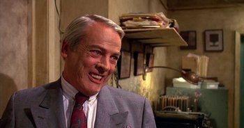 Movie still from “UHF” (1989), directed by Jay Levey – A man in a suit and tie smiling; Close Up shot, Over the shoulder angle