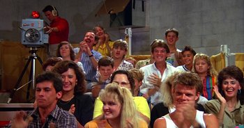 Movie still from “UHF” (1989), directed by Jay Levey – A group of people sitting in front of each other clapping; Medium shot, High angle
