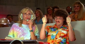 Movie still from “UHF” (1989), directed by Jay Levey – A man and a woman are sitting in front of a crowd; Medium shot, High angle