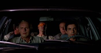Movie still from “UHF” (1989), directed by Jay Levey – A group of people in a car at night; Medium shot, High angle