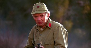 An old man wearing a hat and holding a gun