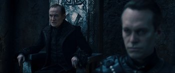 Movie still from “Underworld: Rise of the Lycans” (2009), directed by Patrick Tatopoulos – A man sitting in front of a wall with a camera; Medium shot, Over the shoulder angle