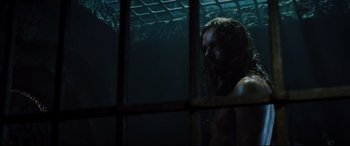 Movie still from “Underworld: Rise of the Lycans” (2009), directed by Patrick Tatopoulos – A man with long hair is standing in a dark room; Medium shot, Over the shoulder angle