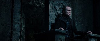 Movie still from “Underworld: Rise of the Lycans” (2009), directed by Patrick Tatopoulos – A man sitting on top of a chair in front of a wall; Medium shot, Low angle