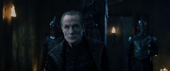 Movie still from “Underworld: Rise of the Lycans” (2009), directed by Patrick Tatopoulos – A man in a black jacket standing next to a statue; Medium shot, Over the shoulder angle