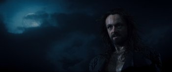 Movie still from “Underworld: Rise of the Lycans” (2009), directed by Patrick Tatopoulos – A man with long hair and a beard is standing in front of a cloudy sky; Close Up shot, Low angle
