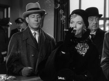 Movie still from “Unfaithfully Yours” (1948), directed by Preston Sturges – An old photo of a woman smoking a cigarette in front of two men; Medium shot, Low angle