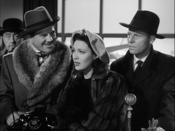 Movie still from “Unfaithfully Yours” (1948), directed by Preston Sturges – A group of people standing next to each other in front of a window; Medium shot, Over the shoulder angle