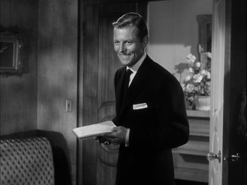 Movie still from “Unfaithfully Yours” (1948), directed by Preston Sturges – A black and white photo of a man in a suit holding a book; Medium shot, Over the shoulder angle