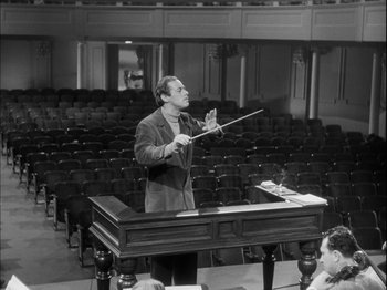 Movie still from “Unfaithfully Yours” (1948), directed by Preston Sturges – A man is conducting an orchestra in an auditorium; Wide shot, High angle