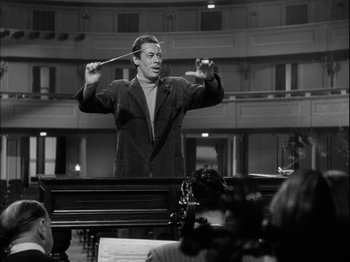Movie still from “Unfaithfully Yours” (1948), directed by Preston Sturges – A man holding a stick while standing in front of an audience; Medium shot, Low angle