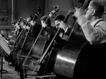 Movie still from “Unfaithfully Yours” (1948), directed by Preston Sturges – A black and white photo of a group of men playing musical instruments; Wide shot, Low angle