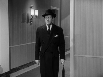 Movie still from “Unfaithfully Yours” (1948), directed by Preston Sturges – A man in a suit and hat holding an umbrella in a hallway; Medium shot, Low angle