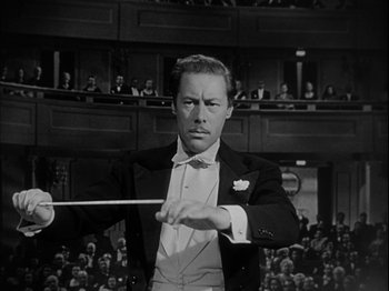 Movie still from “Unfaithfully Yours” (1948), directed by Preston Sturges – A black and white photo of a man in a suit and tie holding a stick; Medium shot, Low angle