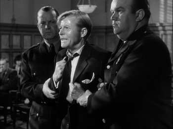 Movie still from “Unfaithfully Yours” (1948), directed by Preston Sturges – A man in a suit and tie standing next to two other men; Medium shot, Over the shoulder angle